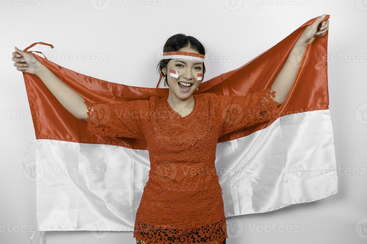 Happy smiling Indonesian woman wearing red kebaya and headband holding Indonesia's flag to celebrate Indonesia Independence Day isolated over white background. photo