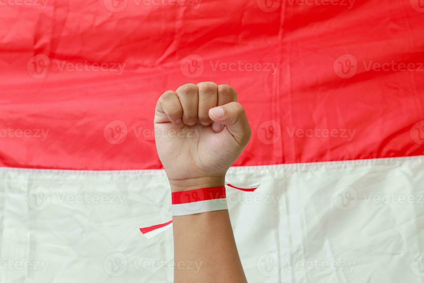 Close up of male hand with red and white ribbon raising up in the air fighting to celebrate Indonesia's independence day. Concept of election movement. photo