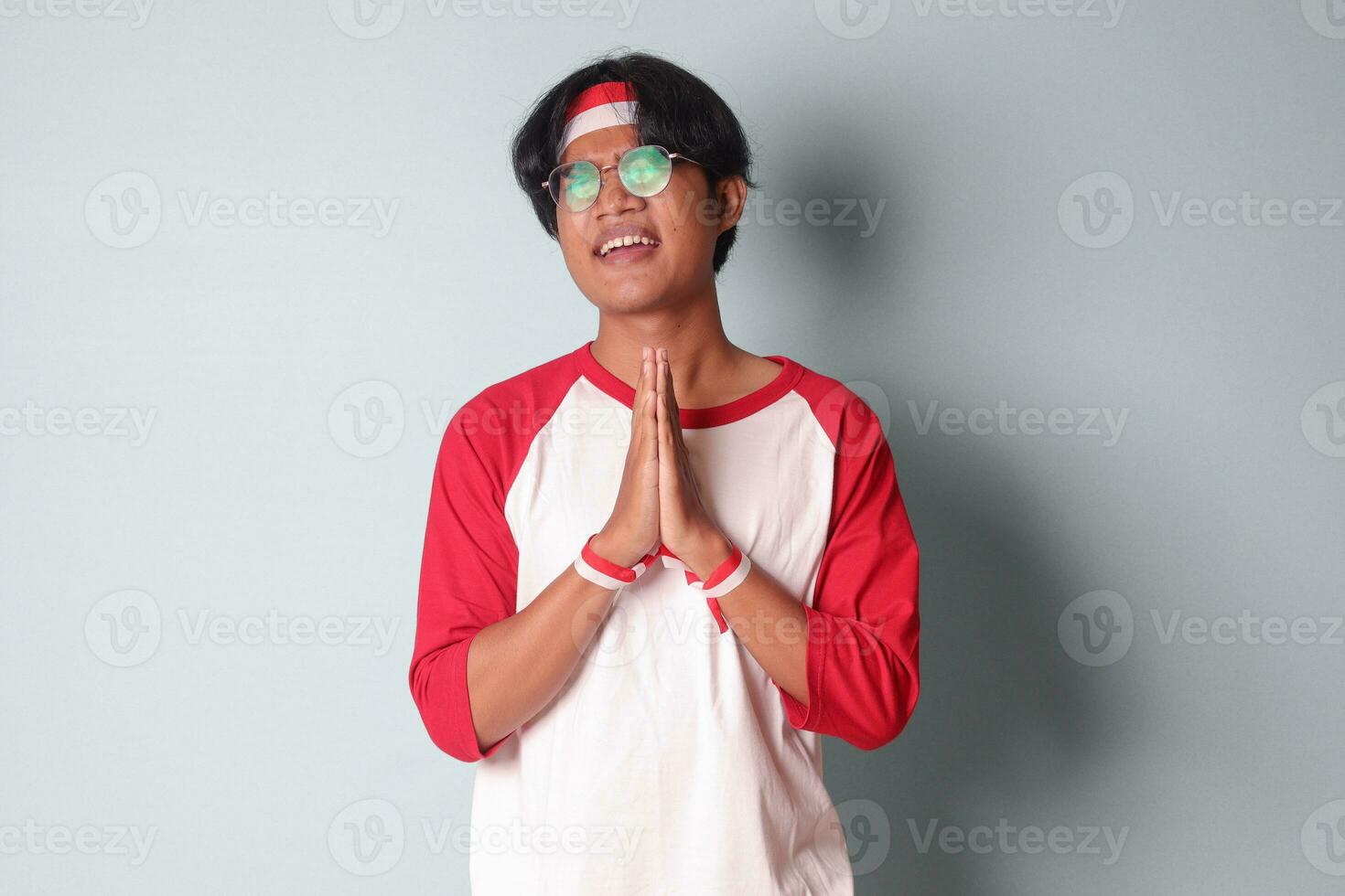Portrait of attractive Asian man in t-shirt with red and white ribbon on head, pulling hands towards camera, inviting someone to come inside, welcoming gesture. Isolated image on gray background photo