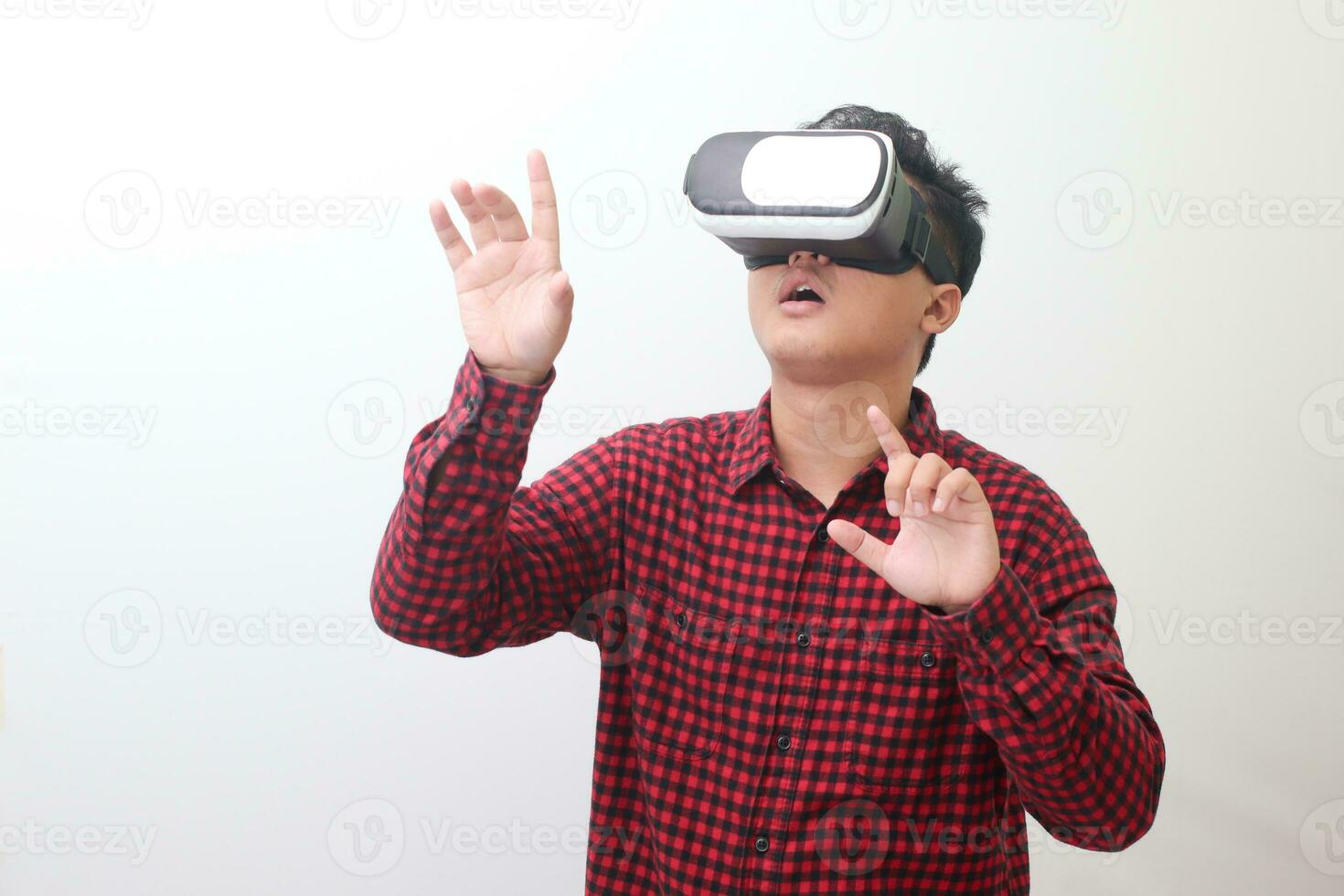 Portrait of Asian man in red plaid shirt using Virtual Reality VR glasses and protecting himself by spreading his arms from something big falling from above. Isolated image on white background photo