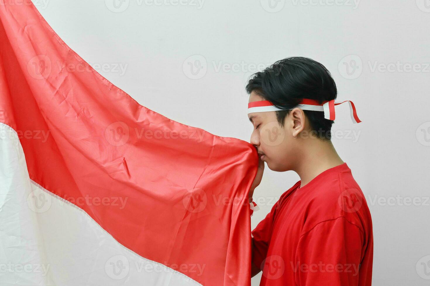 retrato de respetuoso asiático hombre en camiseta con venda cinta en cabeza, besos rojo y blanco bandera de Indonesia. aislado imagen en gris antecedentes foto