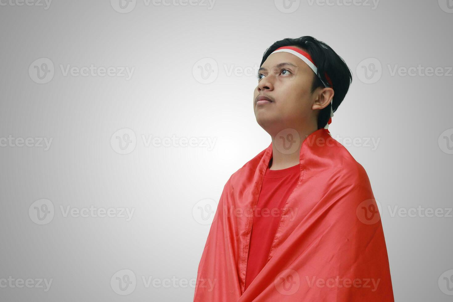 retrato de pensativo asiático hombre en camiseta con rojo blanco cinta en cabeza, abrazado por bandera, celebrando de indonesia independencia día. aislado imagen en gris foto