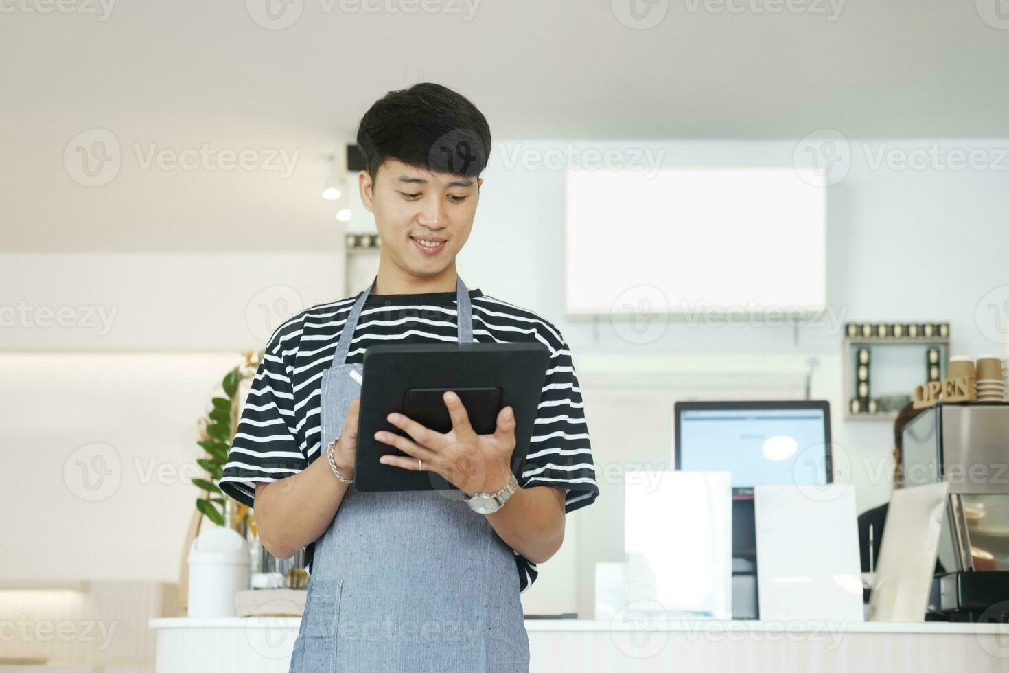 Cheerful young Asian man entrepreneur standing at counter in his own coffee shop photo