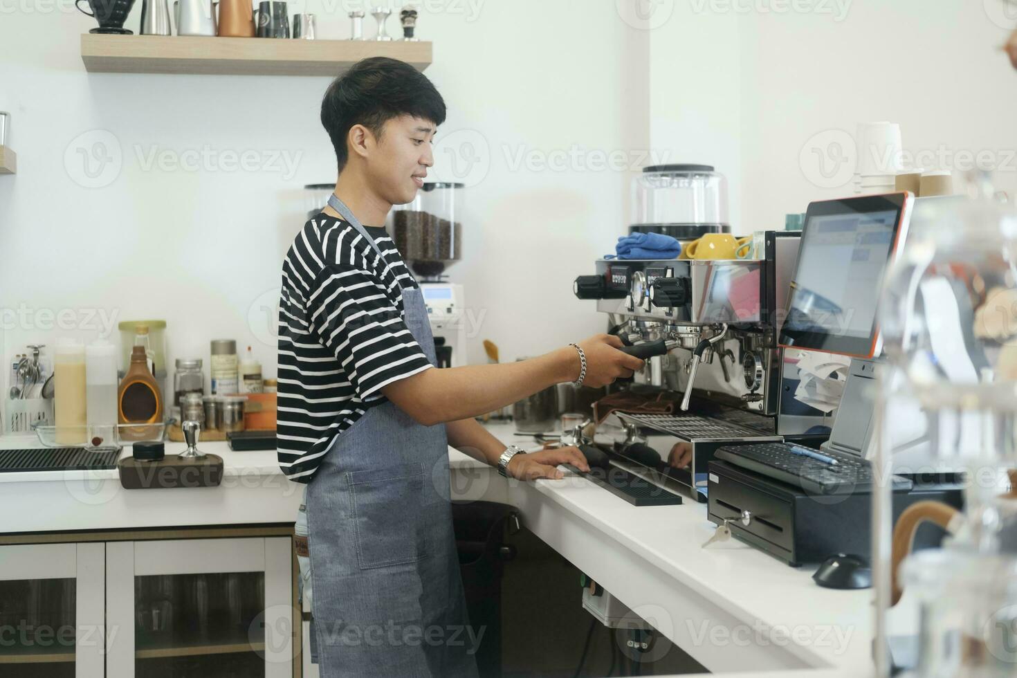 joven alegre barista vistiendo delantal mientras preparando café a un automático máquina en un moderno café tienda. foto