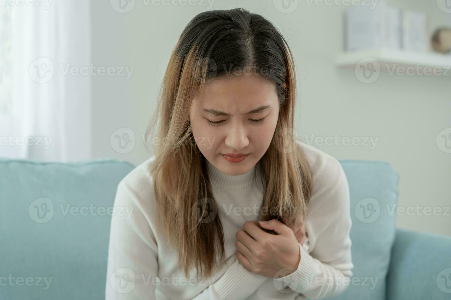 mano sostener cofre con corazón ataque síntomas, asiático mujer trabajando difícil tener cofre dolor causado por corazón enfermedad, filtración, dilatación, engrandecido coronario corazón, prensa en el cofre con doloroso expresión foto