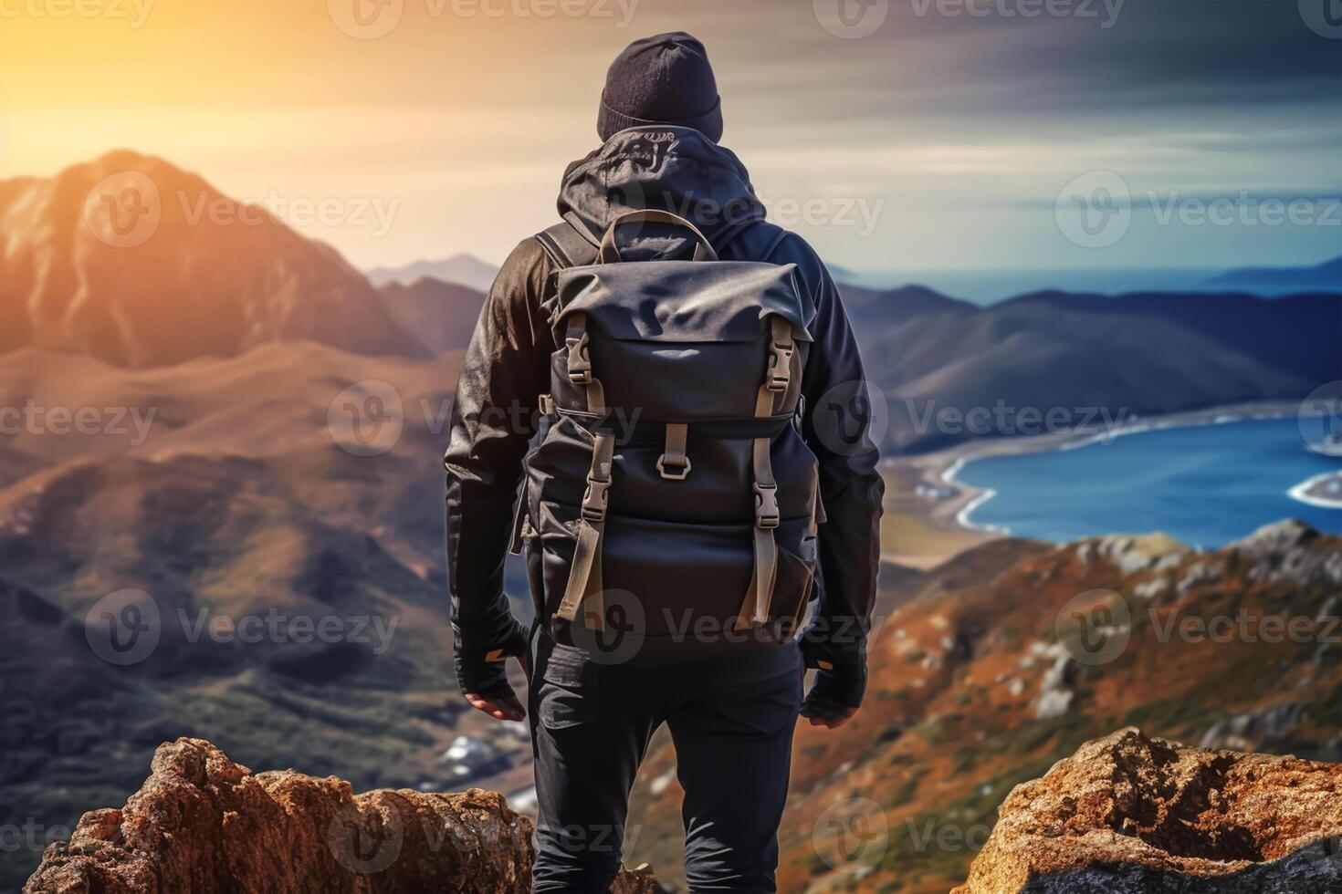 Back view of young man with backpack and hat standing on top of the mountain photo