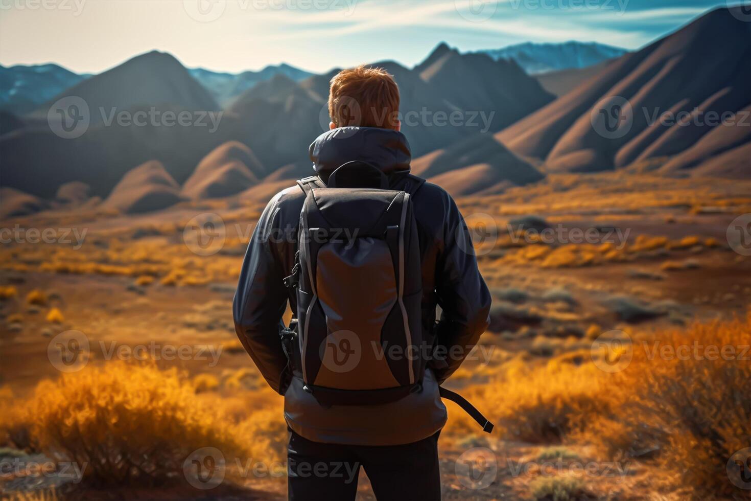 Back view of young man with backpack and hat standing on top of the mountain photo