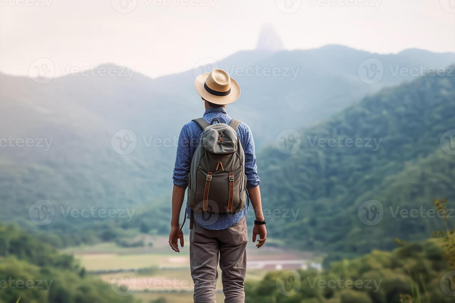 Back view of young man with backpack and hat standing on top of the mountain photo