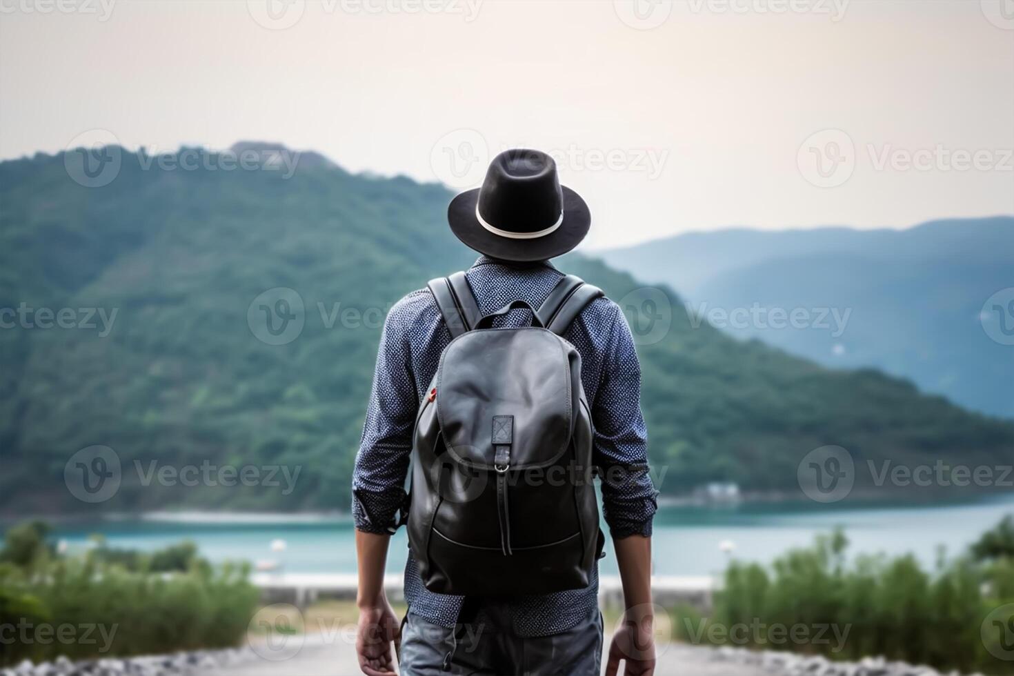 Back view of young man with backpack and hat standing on top of the mountain photo
