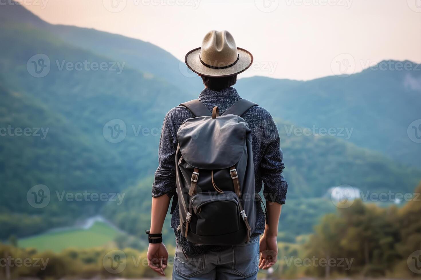 Back view of young man with backpack and hat standing on top of the mountain photo