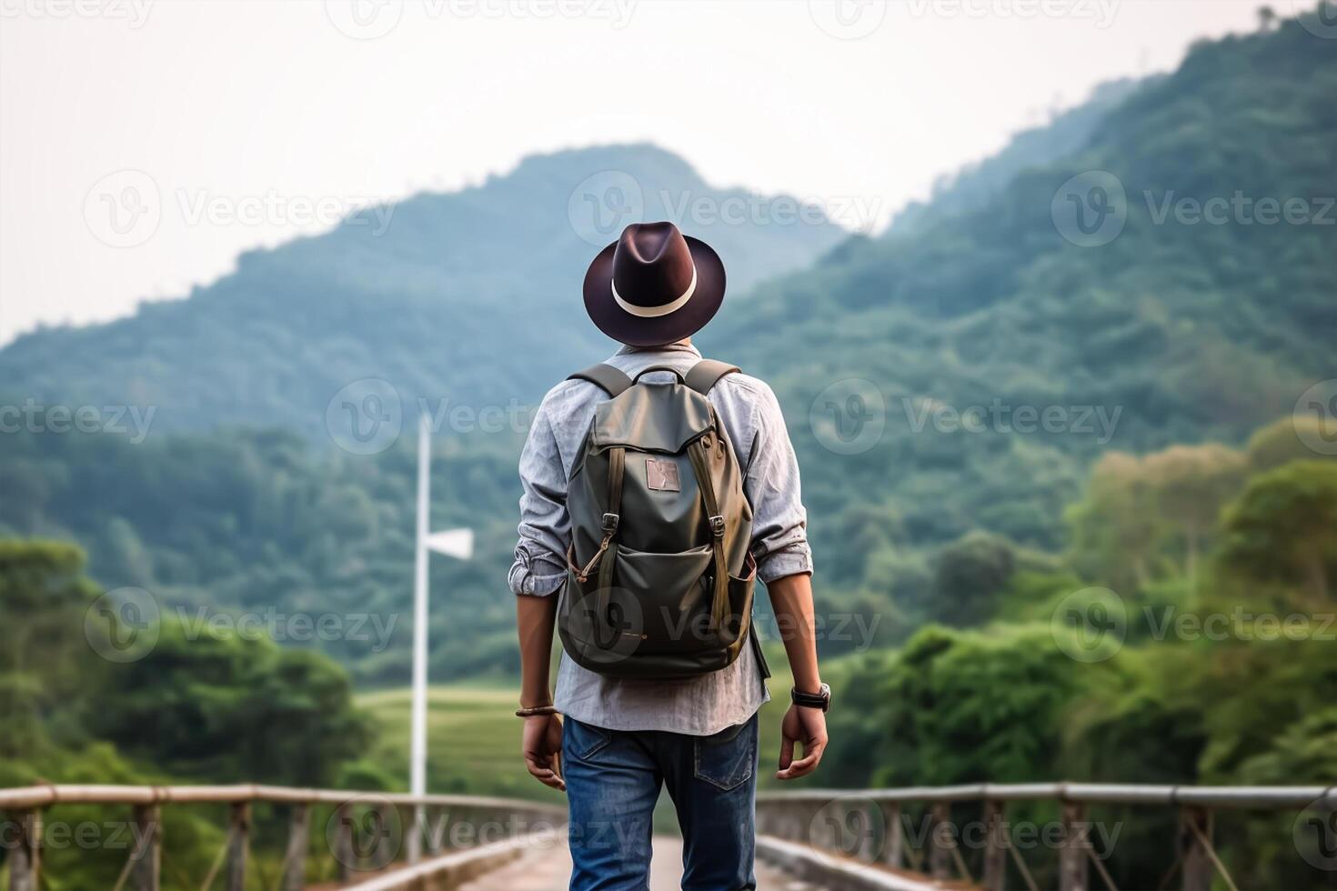 Back view of young man with backpack and hat standing on top of the mountain photo