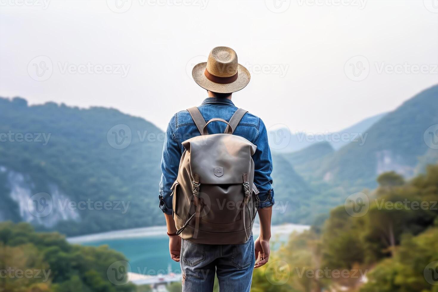 Back view of young man with backpack and hat standing on top of the mountain photo