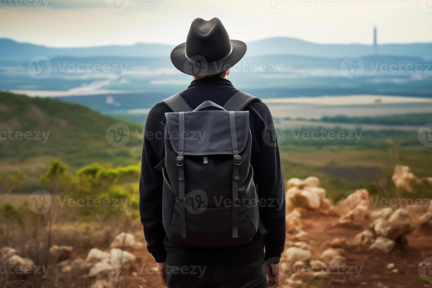 Back view of young man with backpack and hat standing on top of the mountain photo