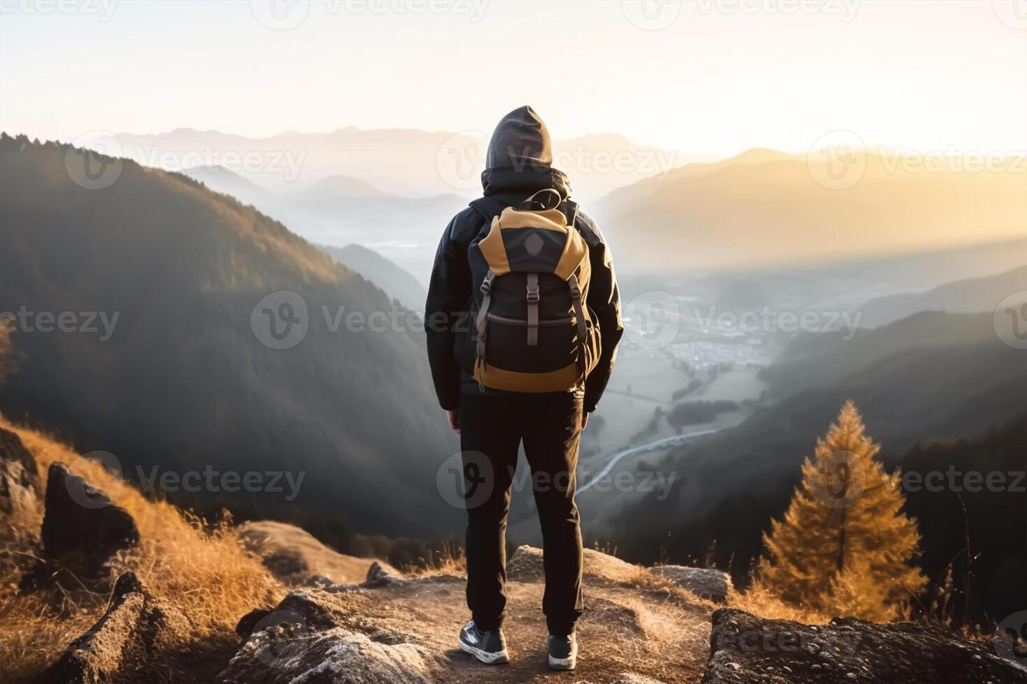 Back view of young man with backpack and hat standing on top of the mountain photo