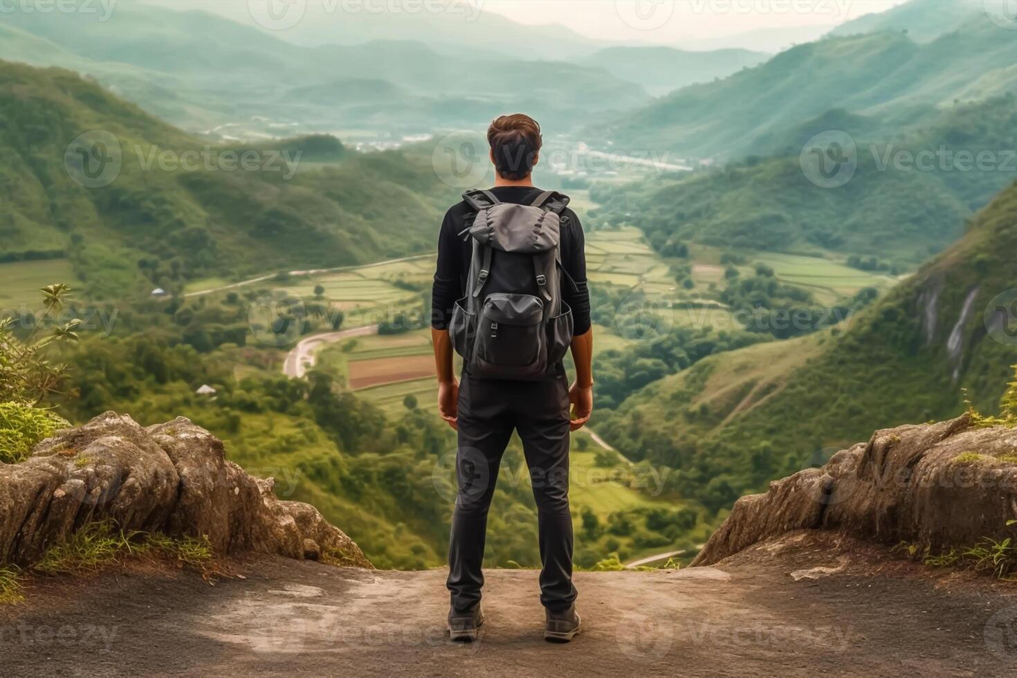 Back view of young man with backpack and hat standing on top of the mountain photo