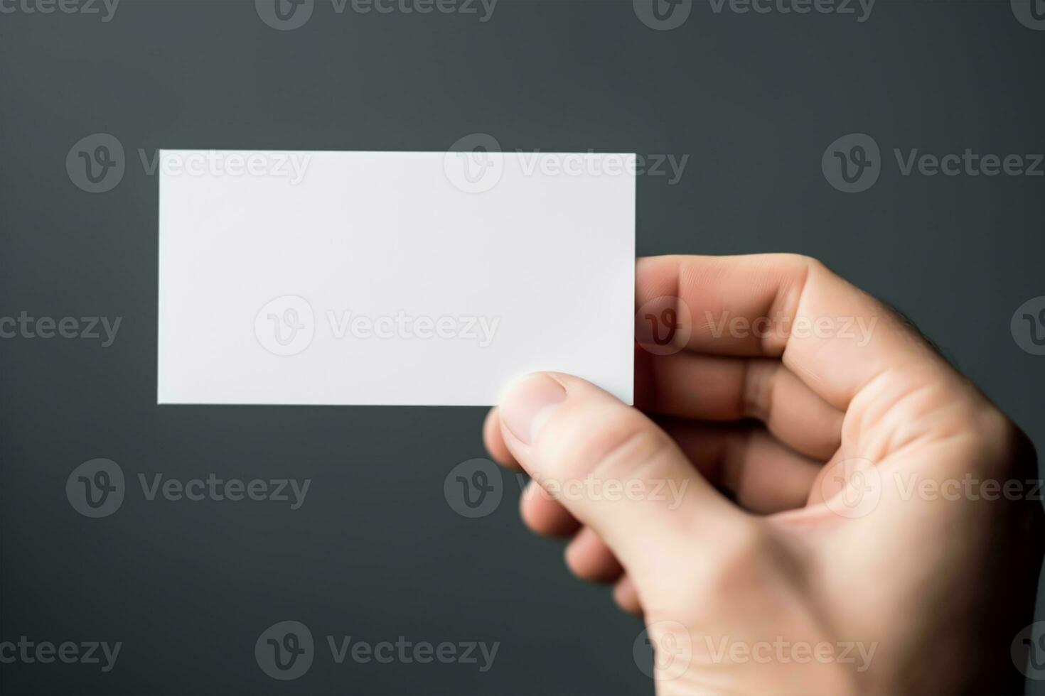 Hand holding a blank business card on a gray background, close up mockup photo