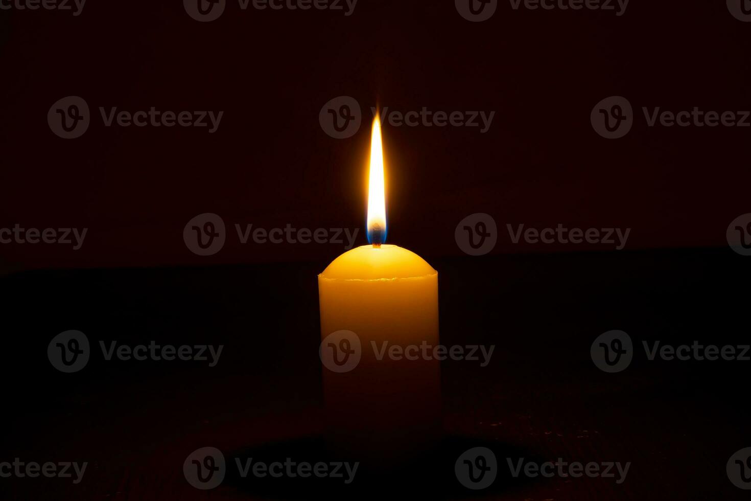 Single burning candle flame or light glowing on a big yellow candle on black or dark background on table in church for Christmas, funeral or memorial service with copy space. photo