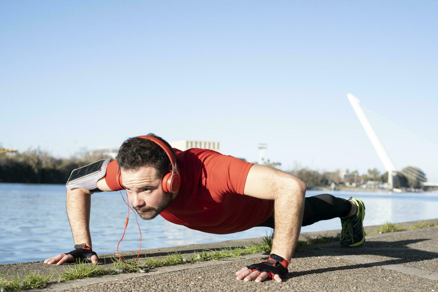 young man doing push-ups with a red t-shirt and music headphones, in an urban environment. healthy living concept photo