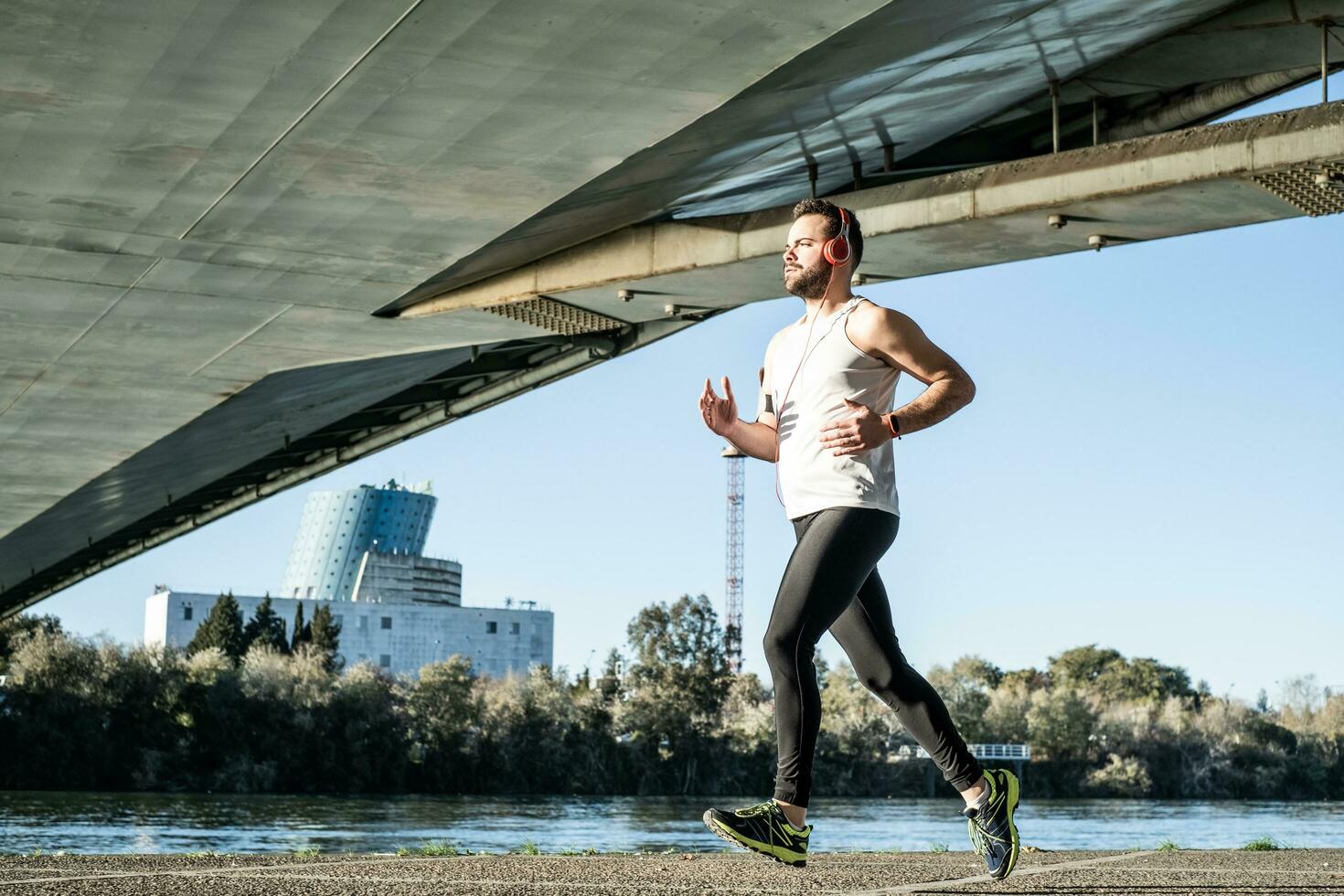 young man running in a white shirt across a bridge. He's listening to music and he's got some helmets on. photo