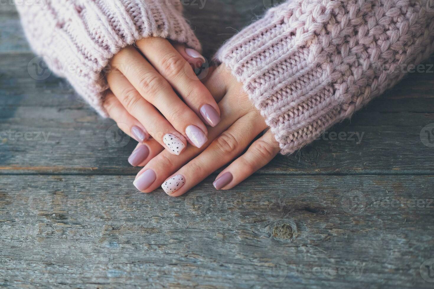 Women is hands with a beautiful manicure  on a wooden background. Autumn trend, polish the beige and quail egg pattern on the nails with gel polish, shellac. Copy space. photo