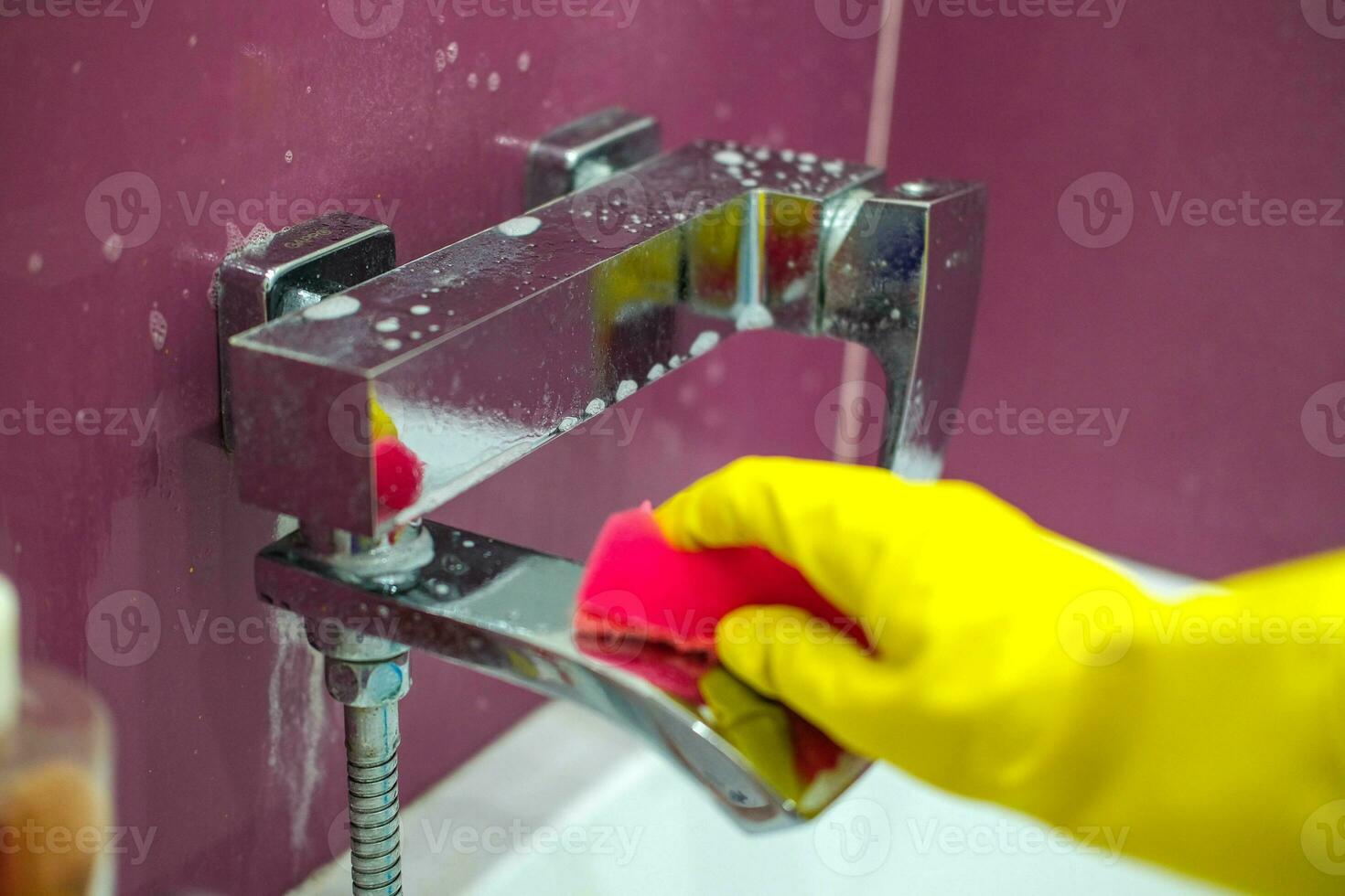 Mixer with cleaning agent. A hand in a rubber glove cleans the faucet with a sponge in the bathroom. photo