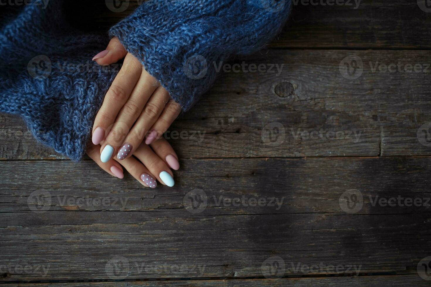 Women is hands with a beautiful manicure, in a knitted sweater on a wooden background in. Autumn trend, polish beige and white polka dots on nails with gel polish, shellac. Close up. photo