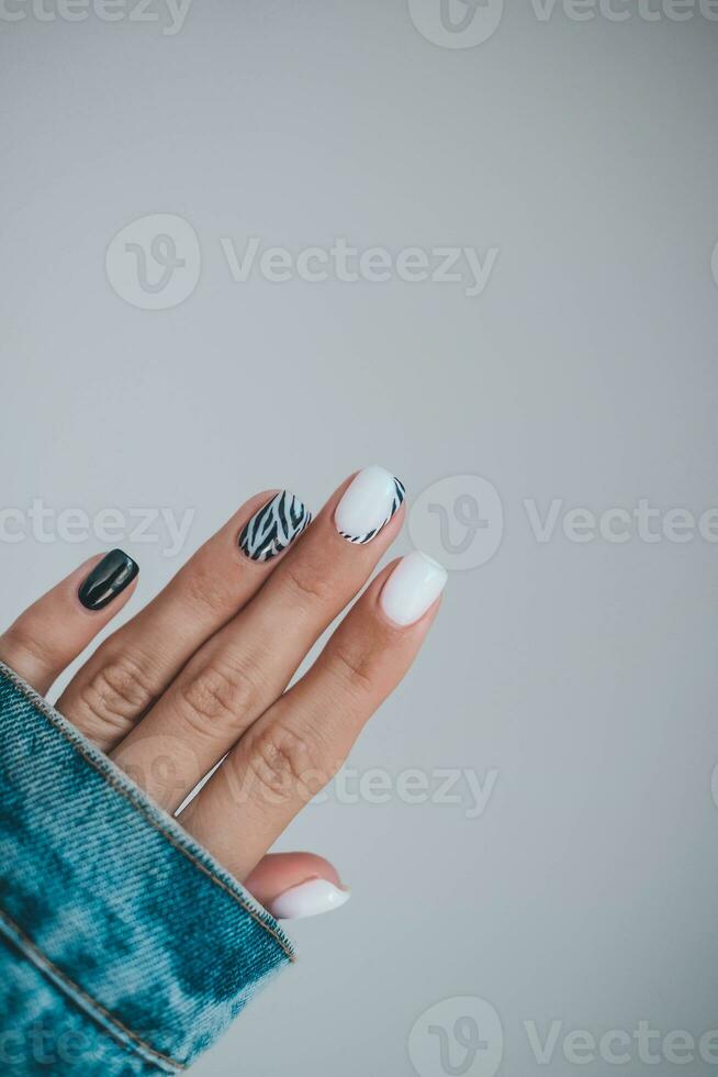 Beautiful female hands with a manicure in a denim jacket. Stylish nail design. Manicure with black and white zebra stripes on the nails. photo