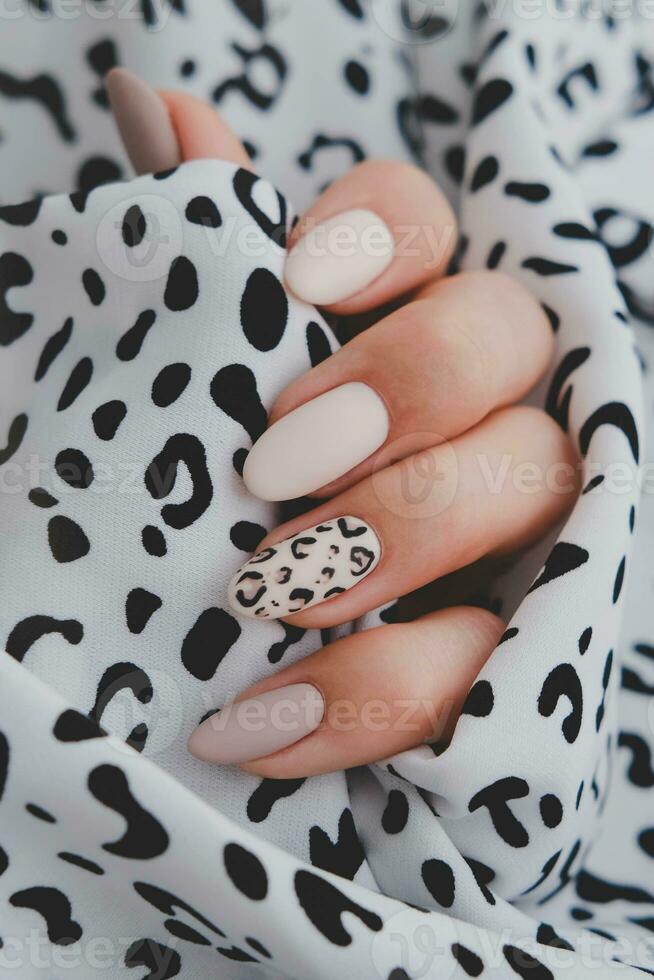 A woman's hand with a beautiful manicure holds a fabric with a leopard print. Autumn trend, beige color polishing with leopard pattern on nails with gel polish, shellac. photo