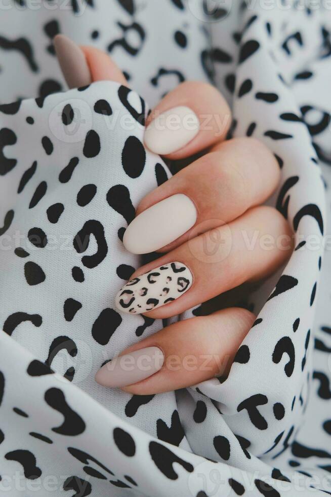 un mujer mano con un hermosa manicura sostiene un tela con un leopardo impresión. otoño tendencia, beige color pulido con leopardo modelo en uñas con gel polaco, goma laca. foto