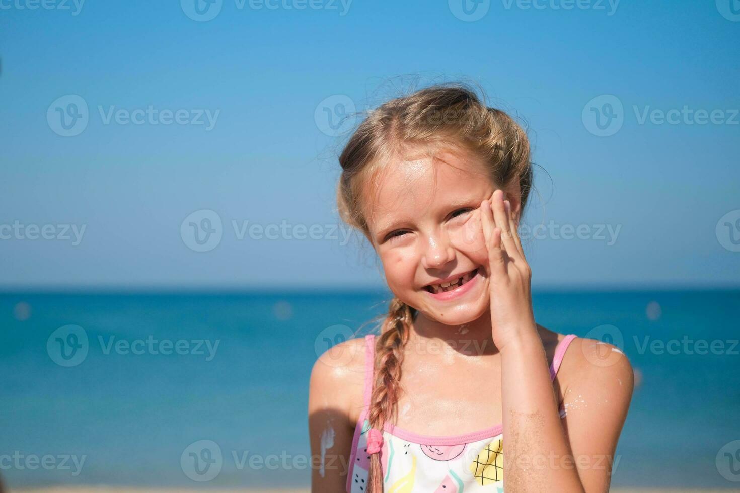 The girl smears her face with sun cream on the sea. photo