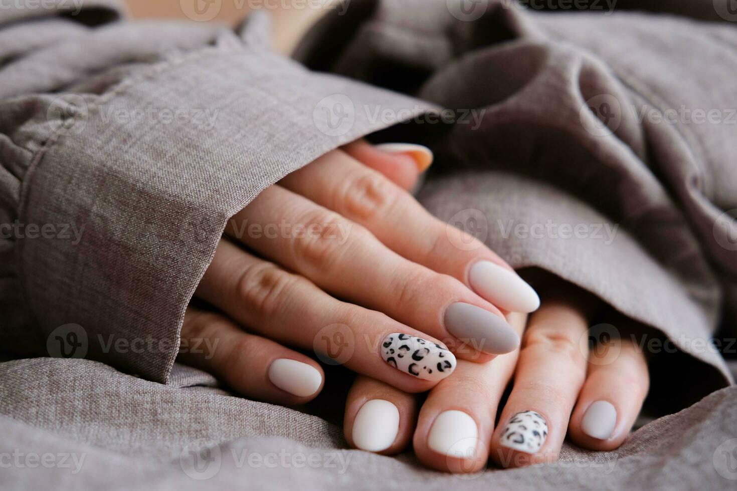 A woman's hand with a beautiful manicure holds a beige fabric. Autumn trend, beige color polishing with leopard pattern on nails with gel polish, shellac. photo