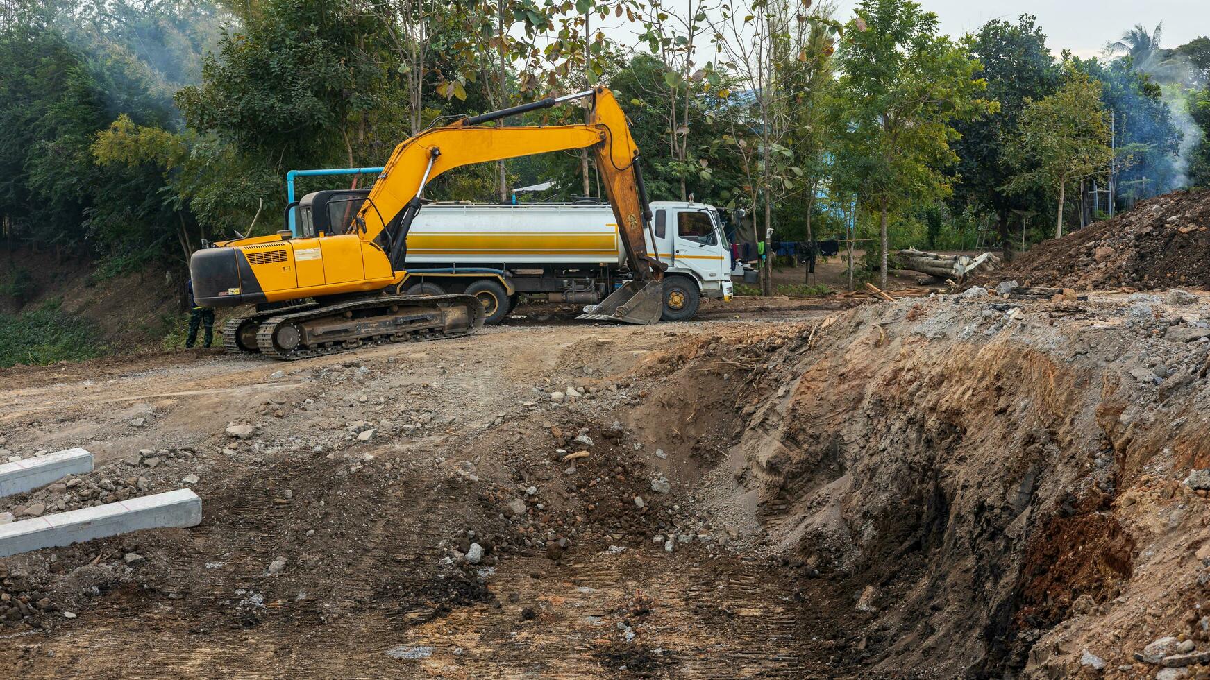 A view of a yellow backhoe and a white water truck stacked on a mound. photo