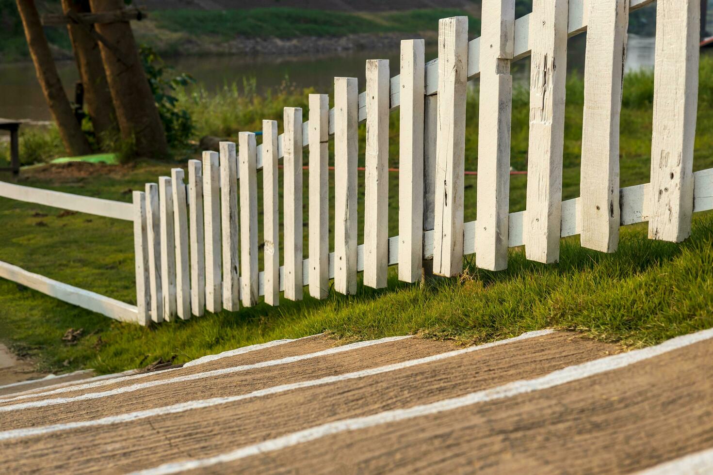 A close-up view of a white wooden fence stretching across the lawn near a concrete staircase. photo