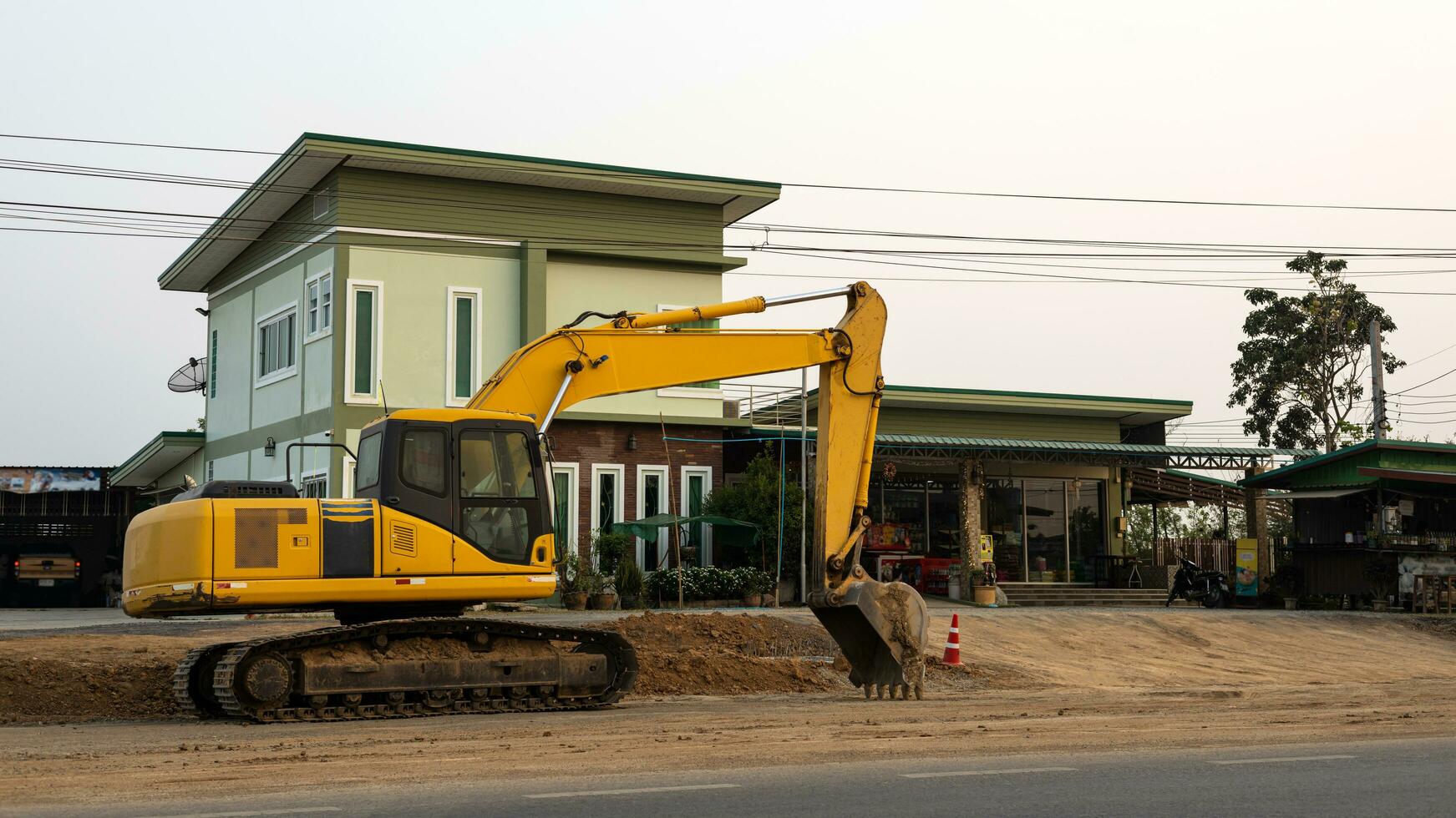 An old yellow backhoe parked on the roadway being renovated near high-voltage power lines. photo