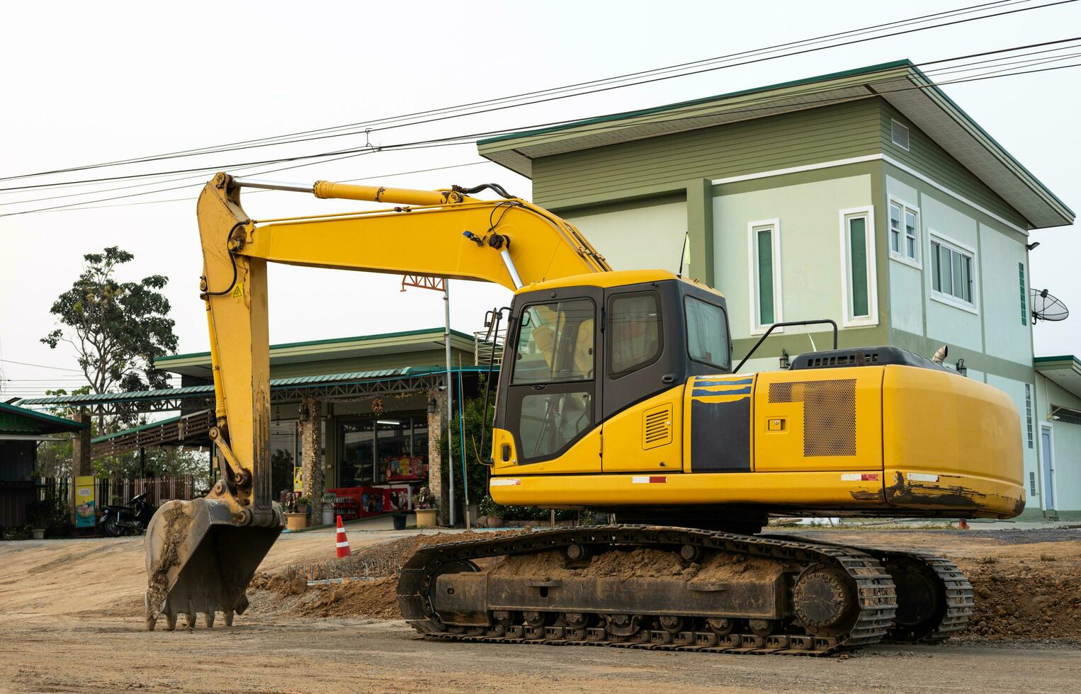 An old yellow backhoe parked on the roadway being renovated near high-voltage power lines. photo