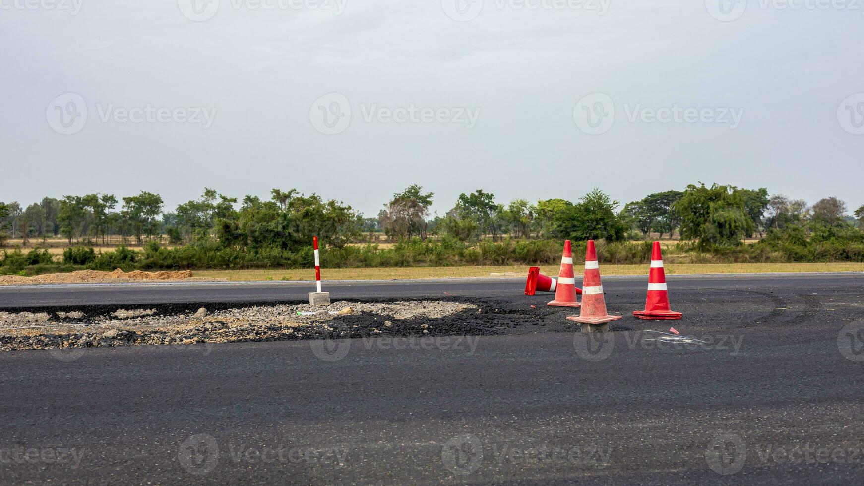 A view of the surface of a new black asphalt road with signs and orange barricades. photo