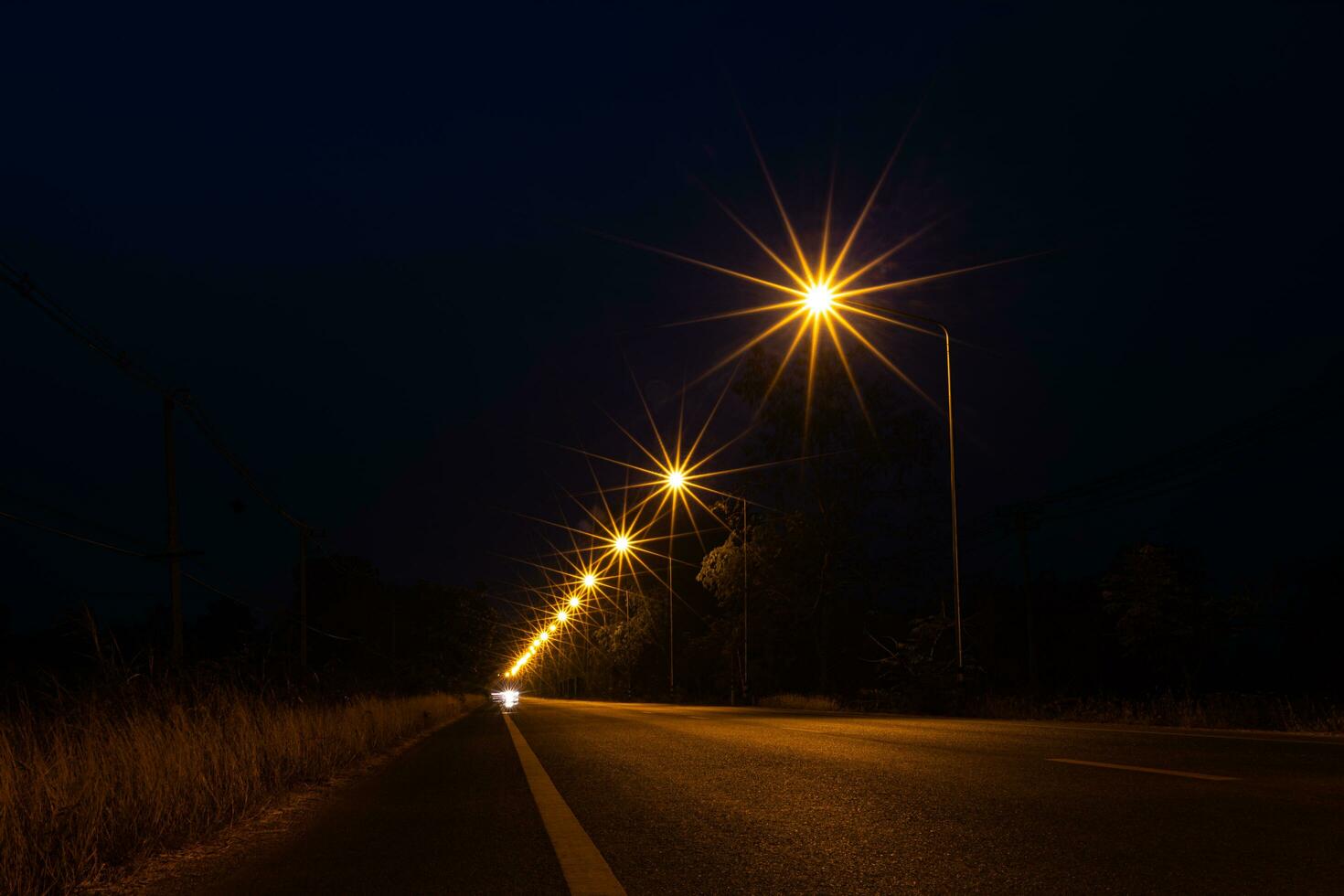 A view of orange starbursts from a lamppost on the side of a street illuminating the tarmac. photo