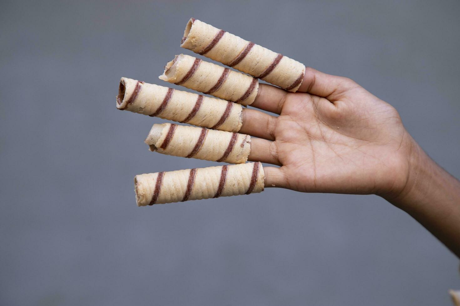 Hand-holding wafer rolls with chocolate on gray background, close up photo