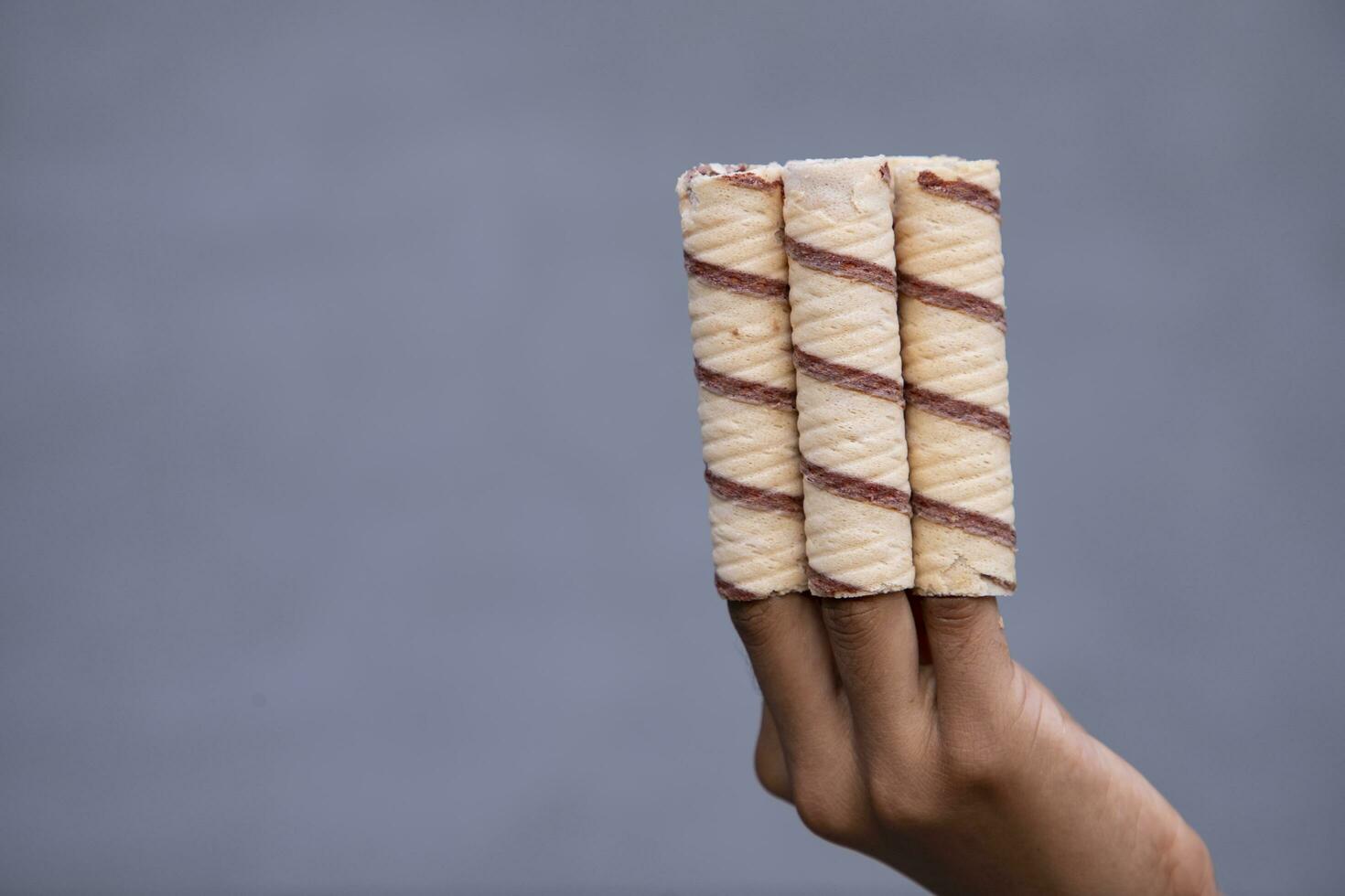 Hand-holding wafer rolls with chocolate on gray background, close up photo