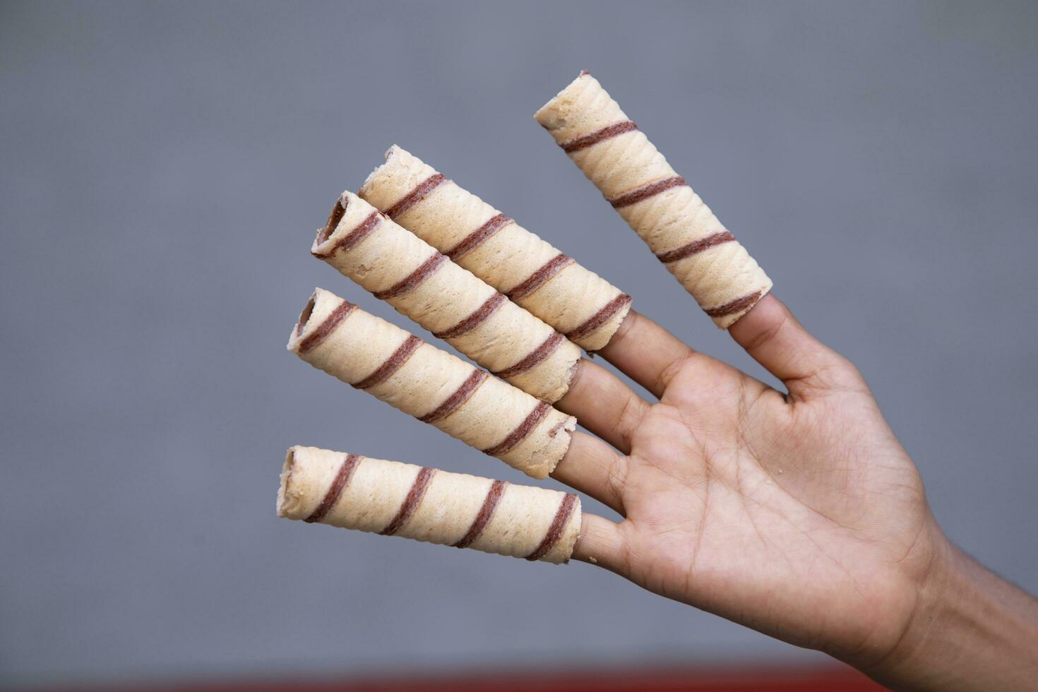 Hand-holding wafer rolls with chocolate on gray background, close up photo