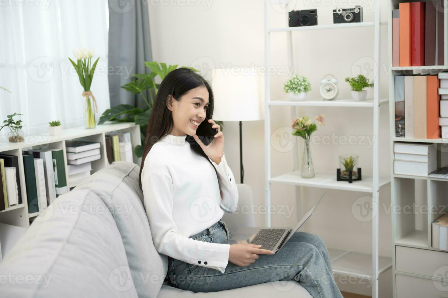 Asian woman using mobile phone with positive expression, big smile, casual dress and sitting on white background sofa. Lovely happy woman congratulating success photo