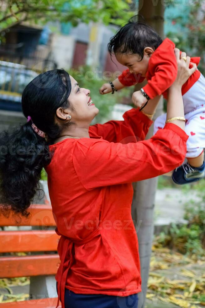 amoroso mamá que lleva de su bebé a sociedad parque. brillante retrato de contento mamá participación niño en su manos. madre abrazando su pequeño 9 9 meses antiguo hijo. foto