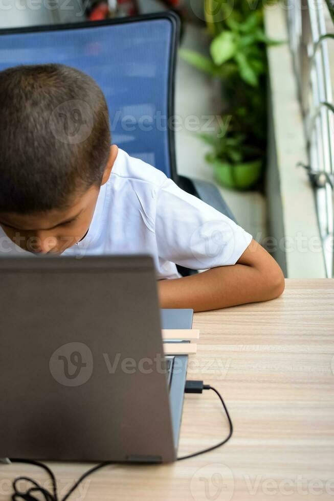 Little boy sitting at table using laptop for online class in Grade 1, Child studying on laptop from home for distance learning online education, School boy children lifestyle concept photo