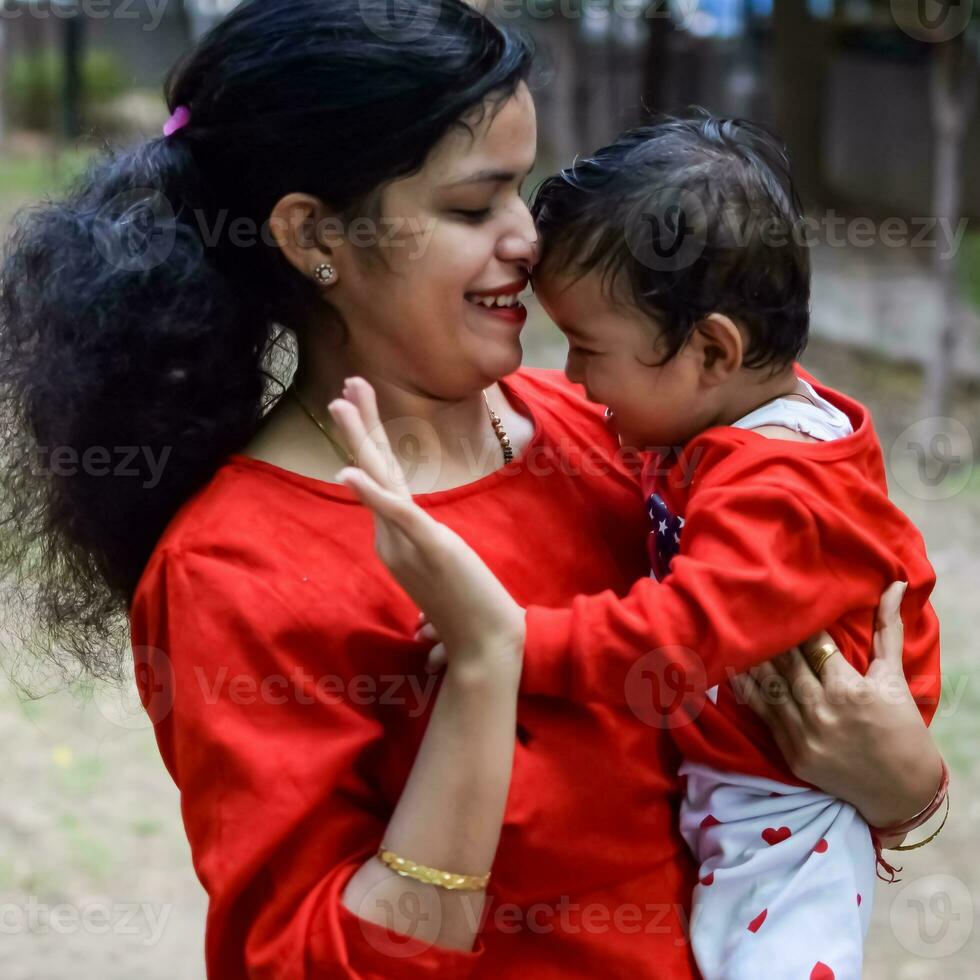 amoroso mamá que lleva de su bebé a sociedad parque. brillante retrato de contento mamá participación niño en su manos. madre abrazando su pequeño 9 9 meses antiguo hijo. foto