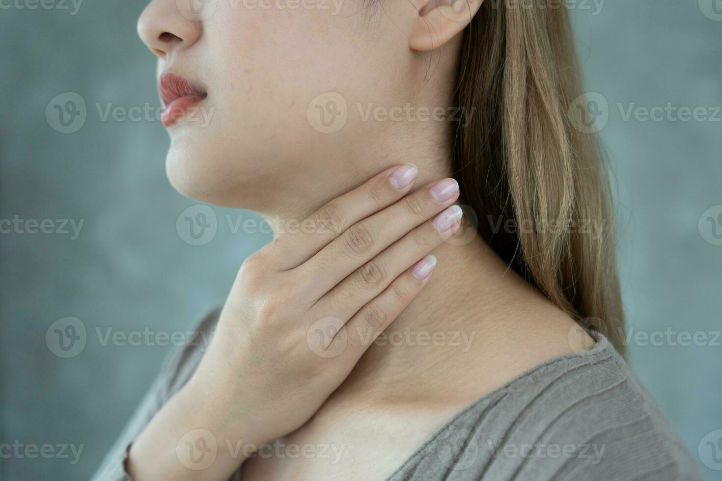 asiático mujer poner su mano en su cuello debido a un dolorido garganta. hembra amigdalitis causas un inflamación. tratado por tomando agua, tomando antibióticos, consultar un doctor, virus, corona virus, influenza, gripe foto