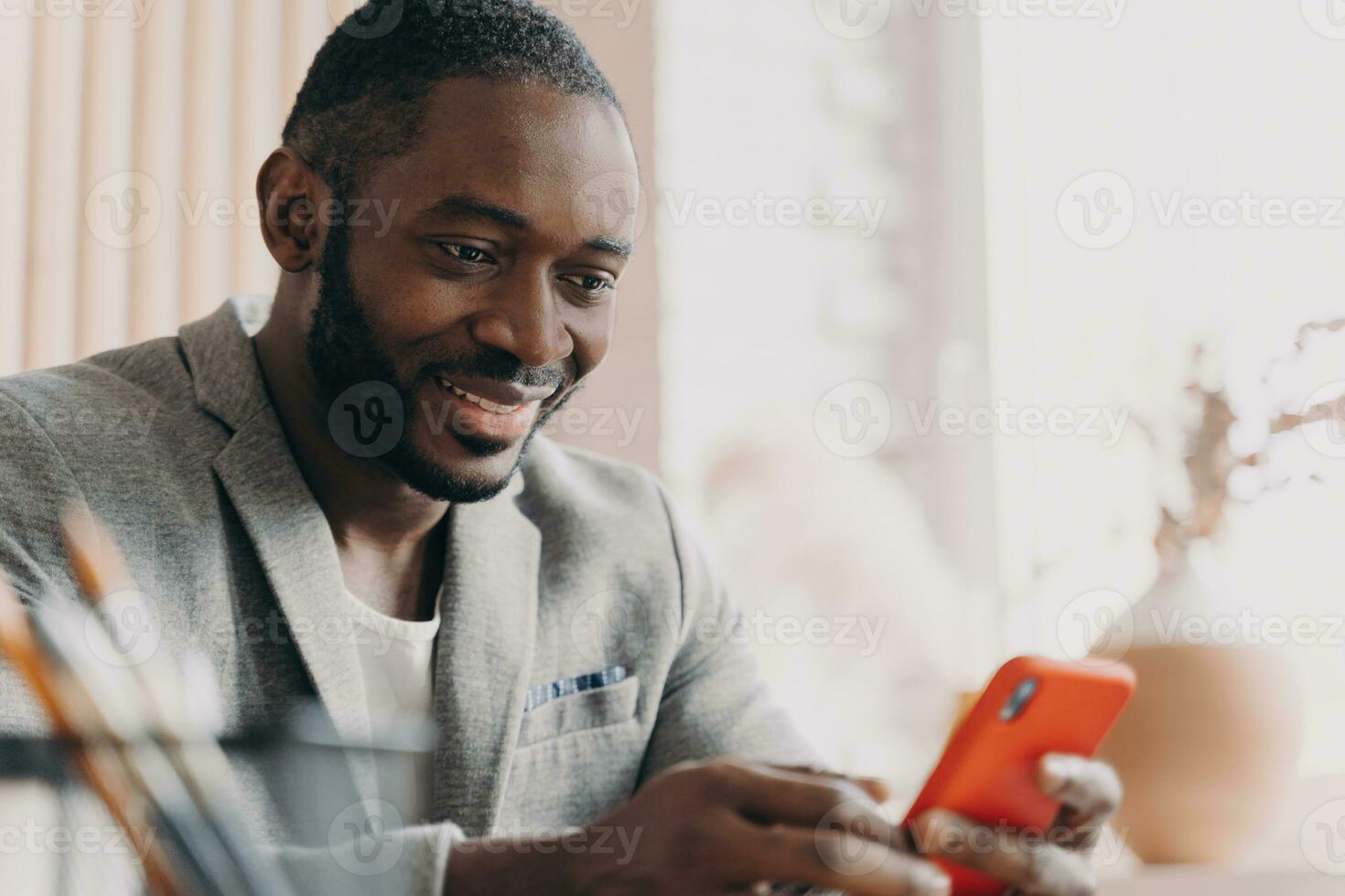 Handsome African American businessman, mobile use, chatting online, office desk, typing message, positive smile, distracted from work. photo