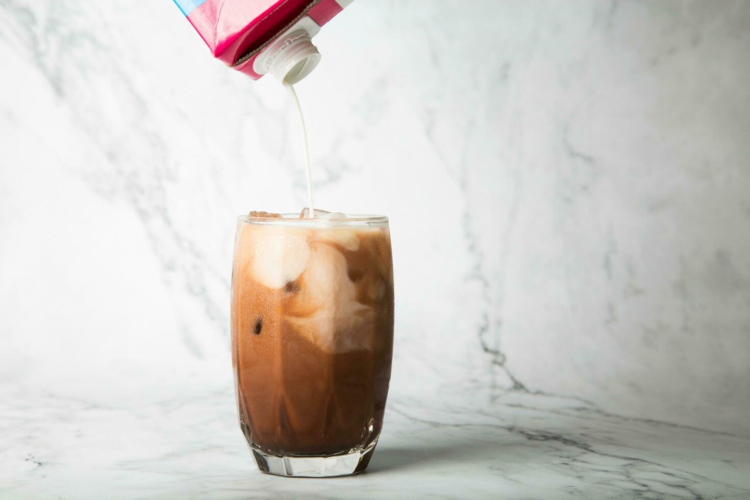 vertido almendra Leche con hielo cacao en claro vaso en mármol, Copiar espacio para tu texto foto