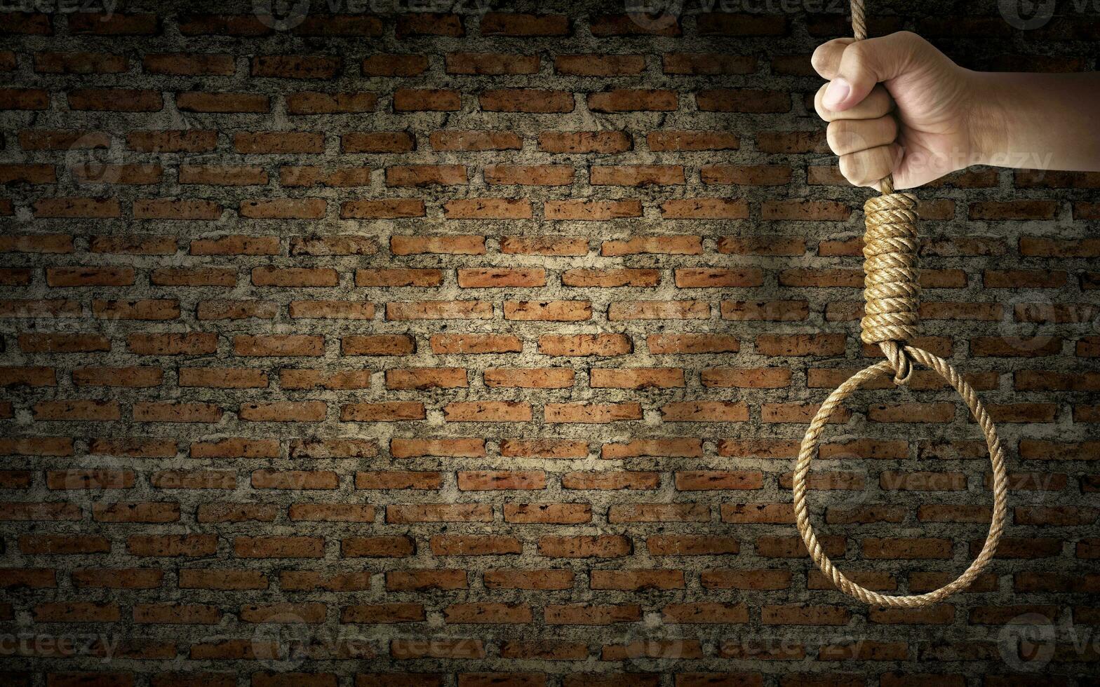 Hand holding rope noose with hangman's knot hanging on dark brick wall photo