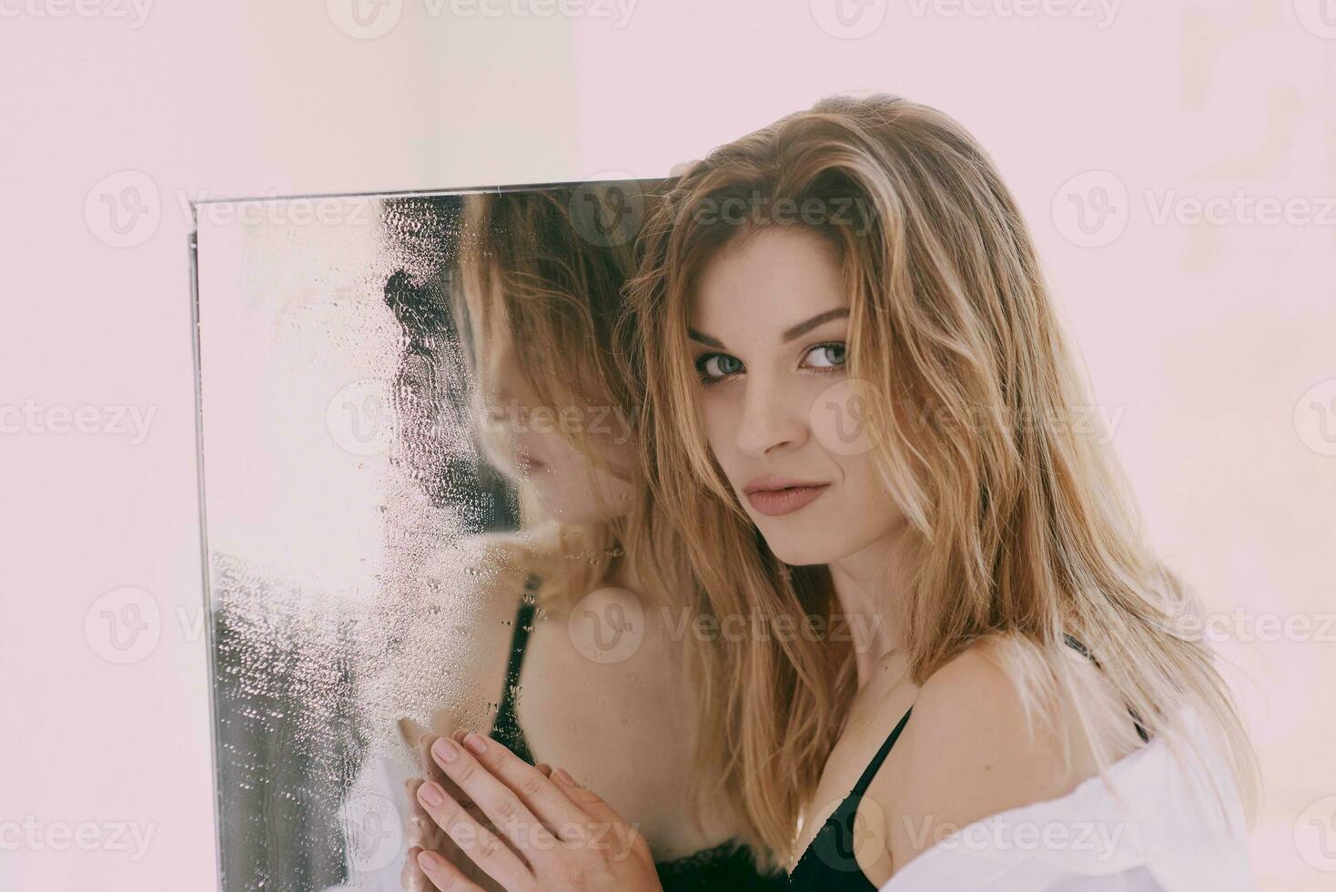 Beautiful caucasian blonde young woman in white shirt standing by the mirror. Health care, beauty, mental issues photo