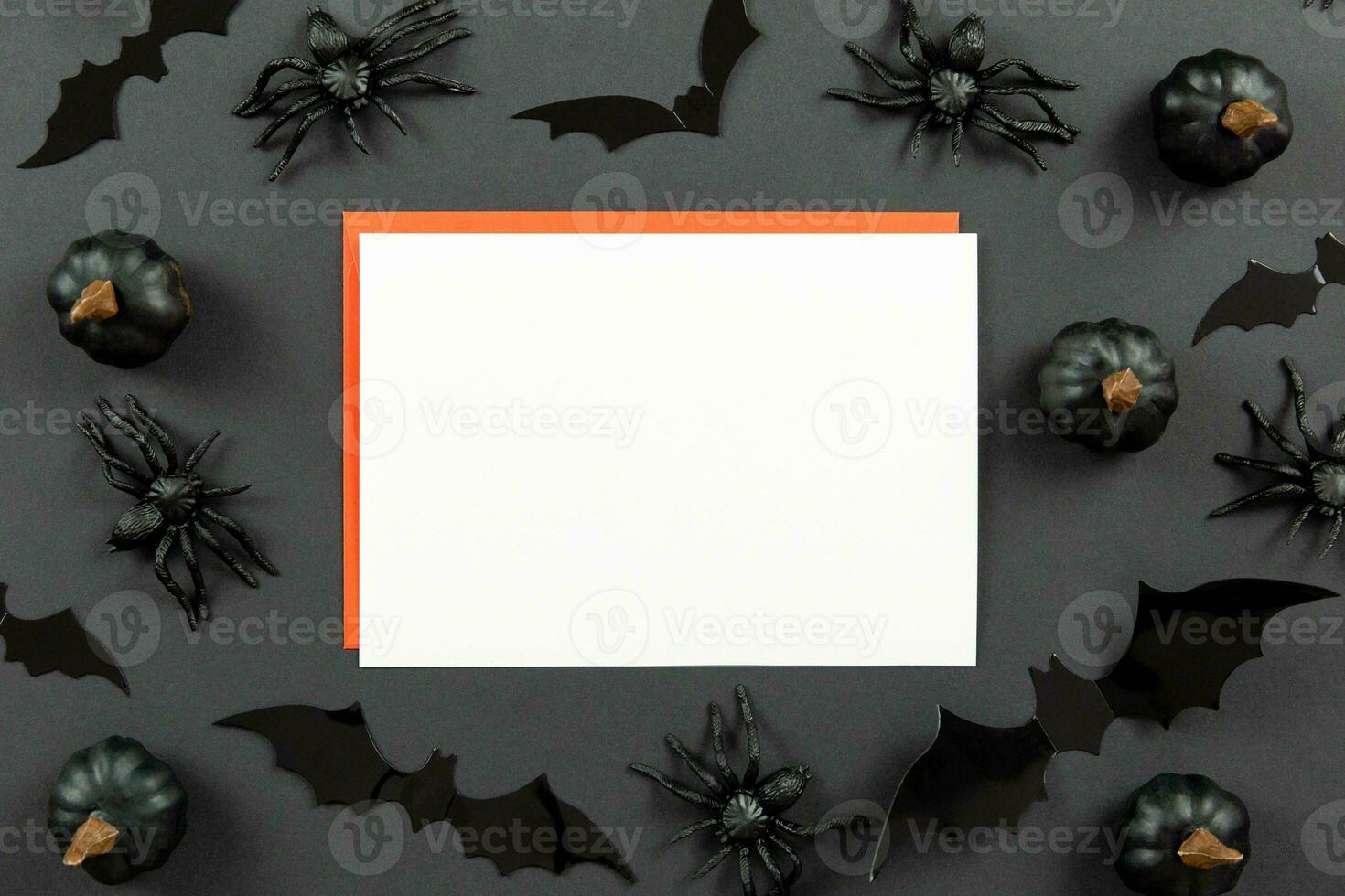 Blank greeting card mockup and red envelopes on dark black background with pumpkins, spiders and bats. Halloween flat lay composition concept. Top view. Copy space. photo